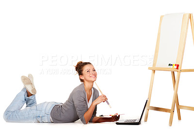 Buy stock photo Shot of smiling young woman lying down by her laptop and a blank canvas on an easel