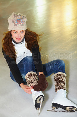 Buy stock photo Portrait of an attractive young woman sitting on an ice rink tying the laces of her ice skates