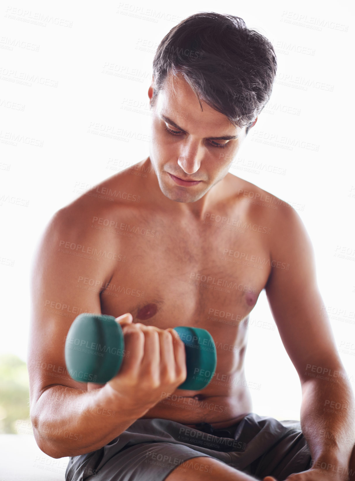 Buy stock photo A muscular young man sitting and lifting dumbbells at home