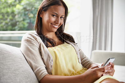 Buy stock photo Shot of an attractive young woman using her mobile phone while relaxing on the sofa