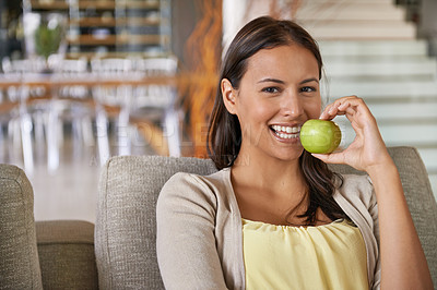 Buy stock photo Portrait of an attractive young woman eating an apple while relaxing on a sofa