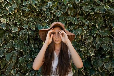 Buy stock photo Woman, portrait and confidence by hedge outdoor with travel, summer holiday and casual fashion with hat. Girl, face and serious at leaf fence in garden for relax, wellness and confidence in Amsterdam