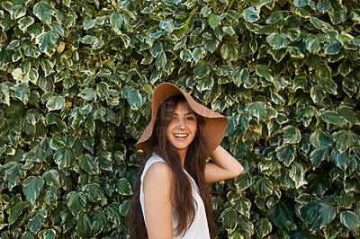 Buy stock photo Woman, portrait and happiness by hedge outdoor with travel, summer holiday and casual fashion with hat. Girl, face and smile at leaf fence in garden for relax, wellness and confidence in Amsterdam