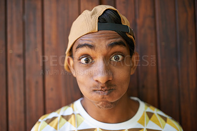 Buy stock photo Portrait of a teenage boy making a face while standing against a wooden wall