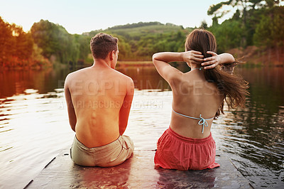 Buy stock photo Relax, calm and couple on pier at lake together for holiday adventure in nature from back. Vacation, young woman and man at water with morning chat, summer and outdoor conversation on dock at river