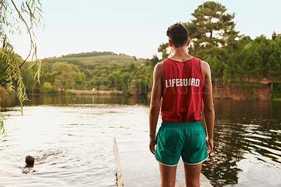 Buy stock photo Back view, teenager and lifeguard outdoor at lake, river and working for safety, security and health of friends swimming. Young man, male person and youth in nature, forest and environment with water