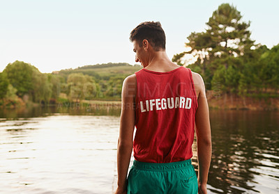 Buy stock photo Rear view shot of teenage boy wearing a lifeguard shirt looking out onto a lake