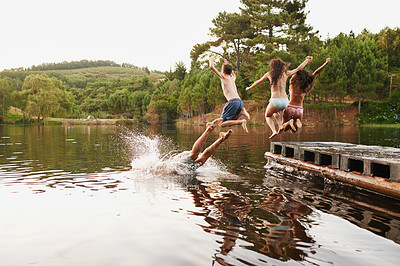 Buy stock photo Shot of a group of teenage friends jumping off a pier into a lake