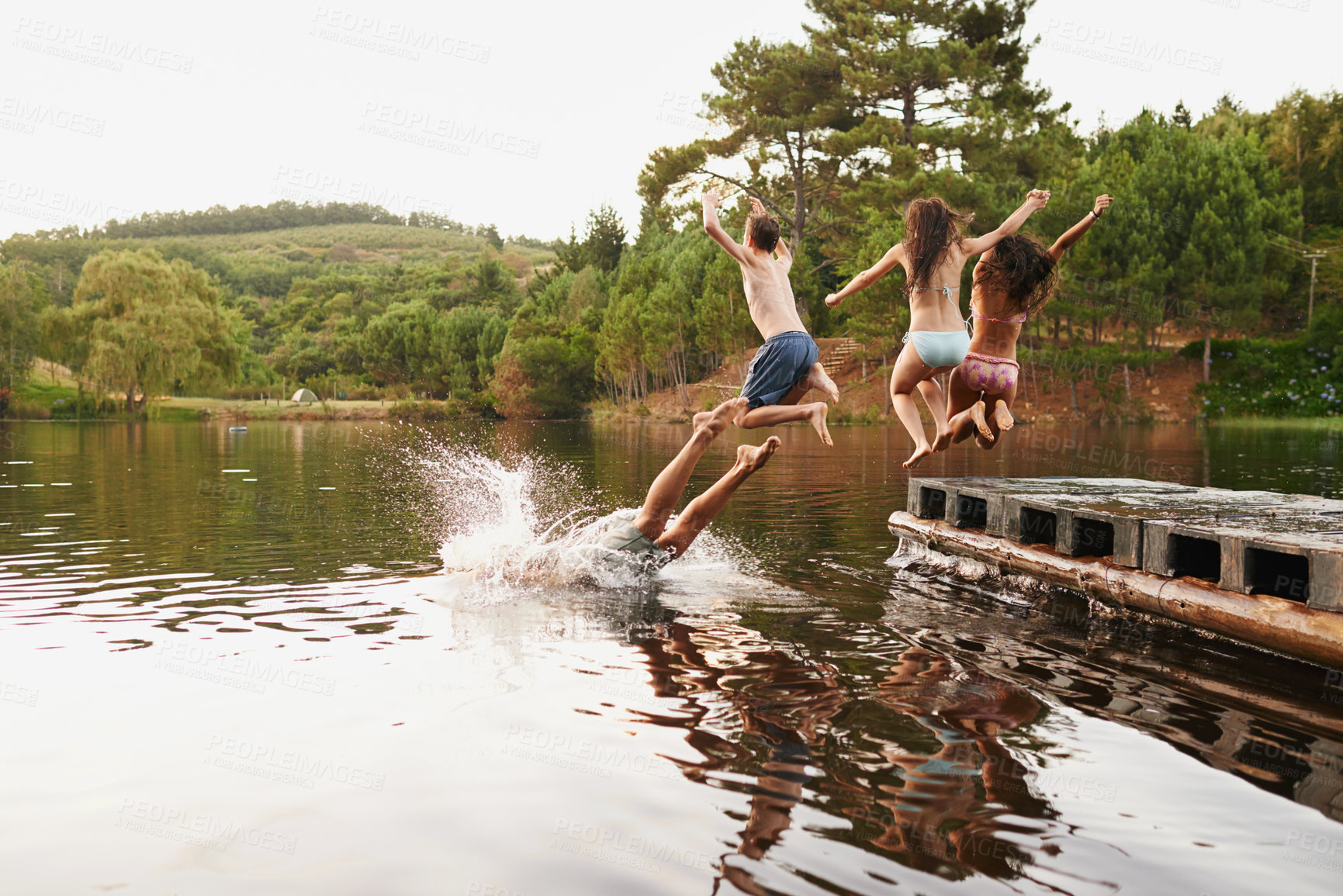 Buy stock photo Shot of a group of teenage friends jumping off a pier into a lake