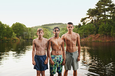 Buy stock photo Portrait, young men and friends in swimwear by lake, river and water outdoor in nature, landscape and forest. Group, teenage boys and diversity on vacation, holiday and camping trip for summer
