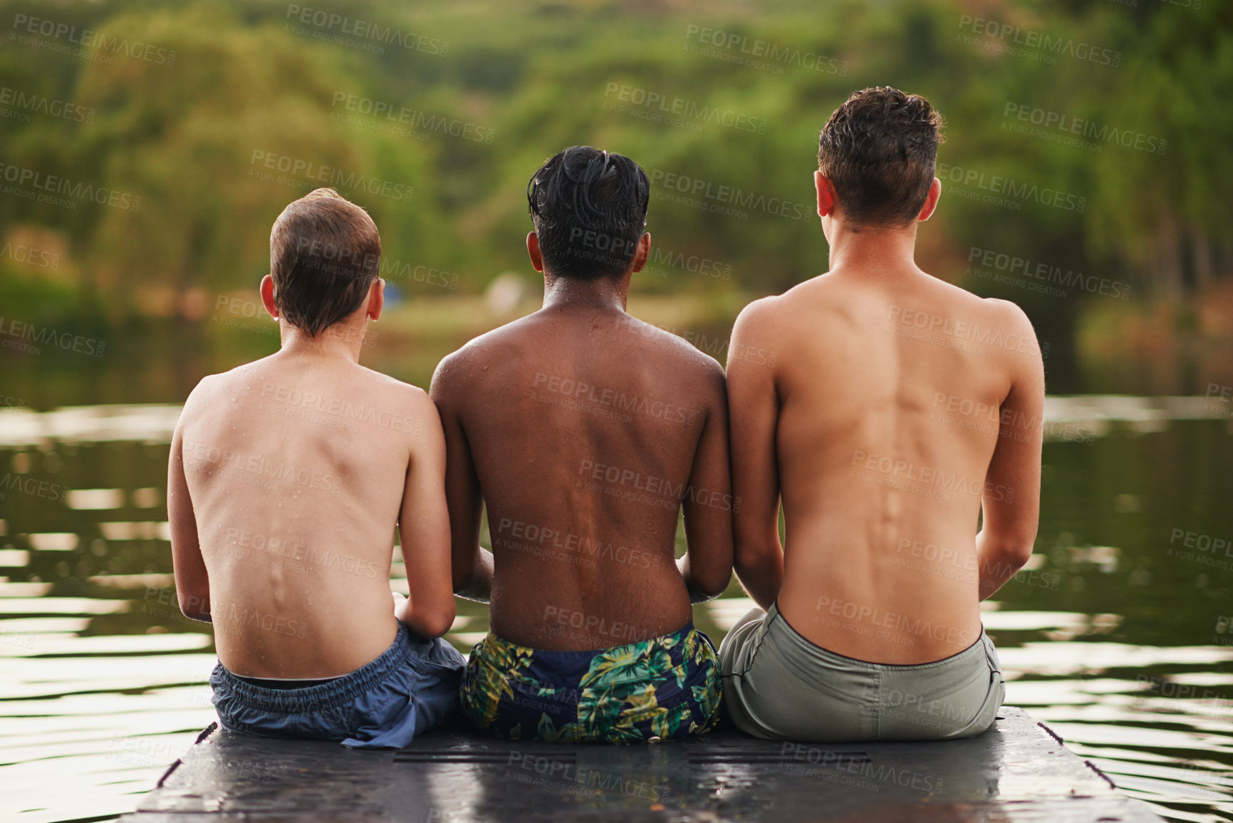 Buy stock photo Rear view shot of three teenage boys sitting on the edge of a pier on a lake