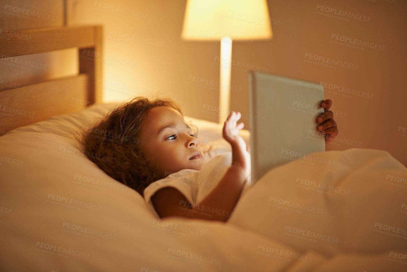 Buy stock photo A cute little girl lying in a double bed and playing on a tablet