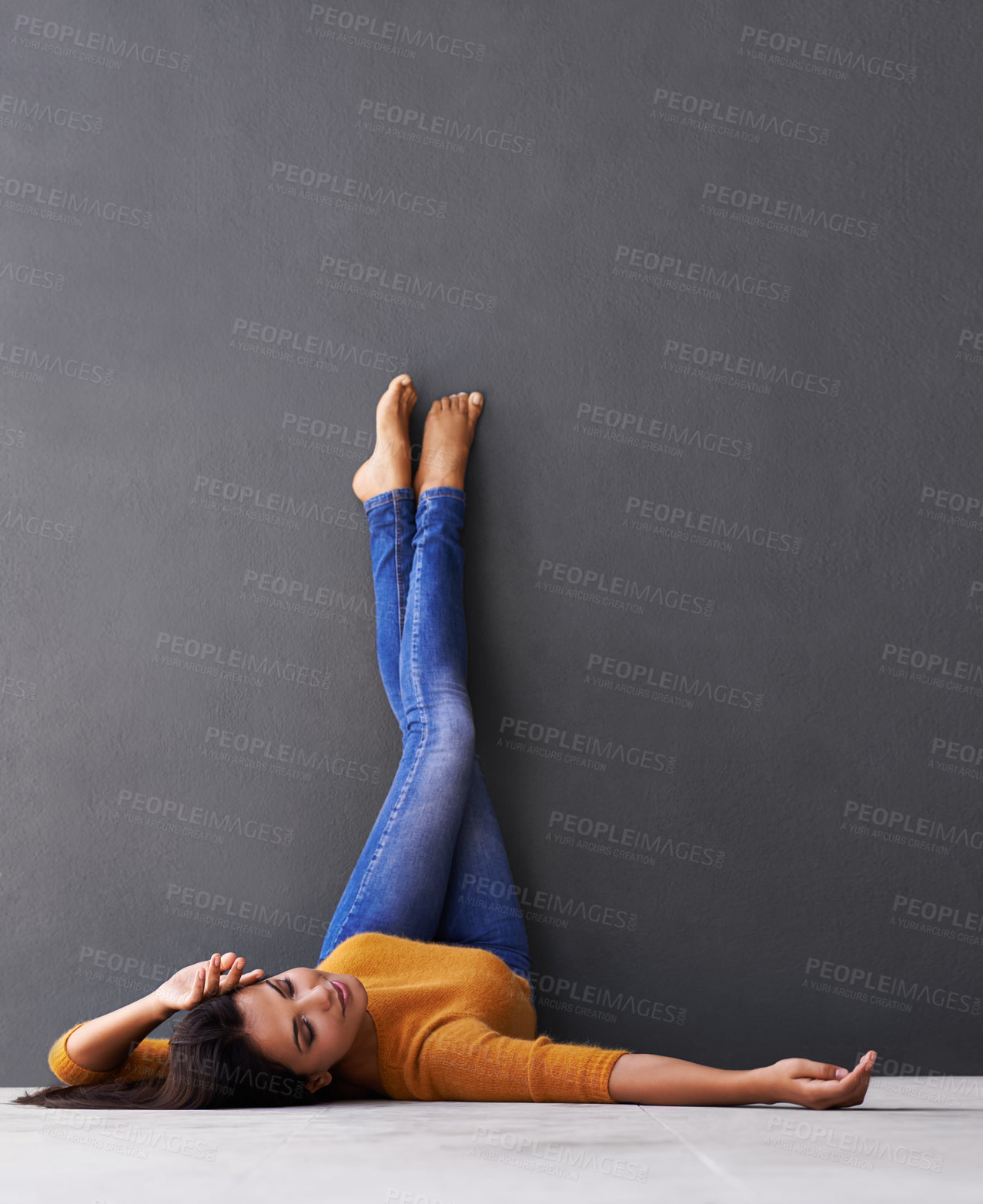 Buy stock photo Woman, style and wall background for laying, feet and relaxing on floor in sleep with fashion. Female person, positive and chill at home for happiness, casual and wellness in jeans with toes in air