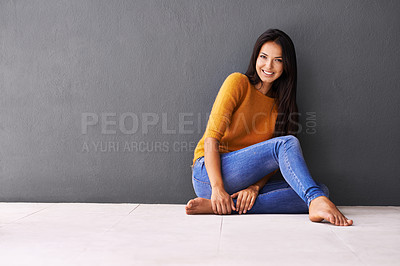 Buy stock photo Portrait of an attractive young woman sitting against a gray wall