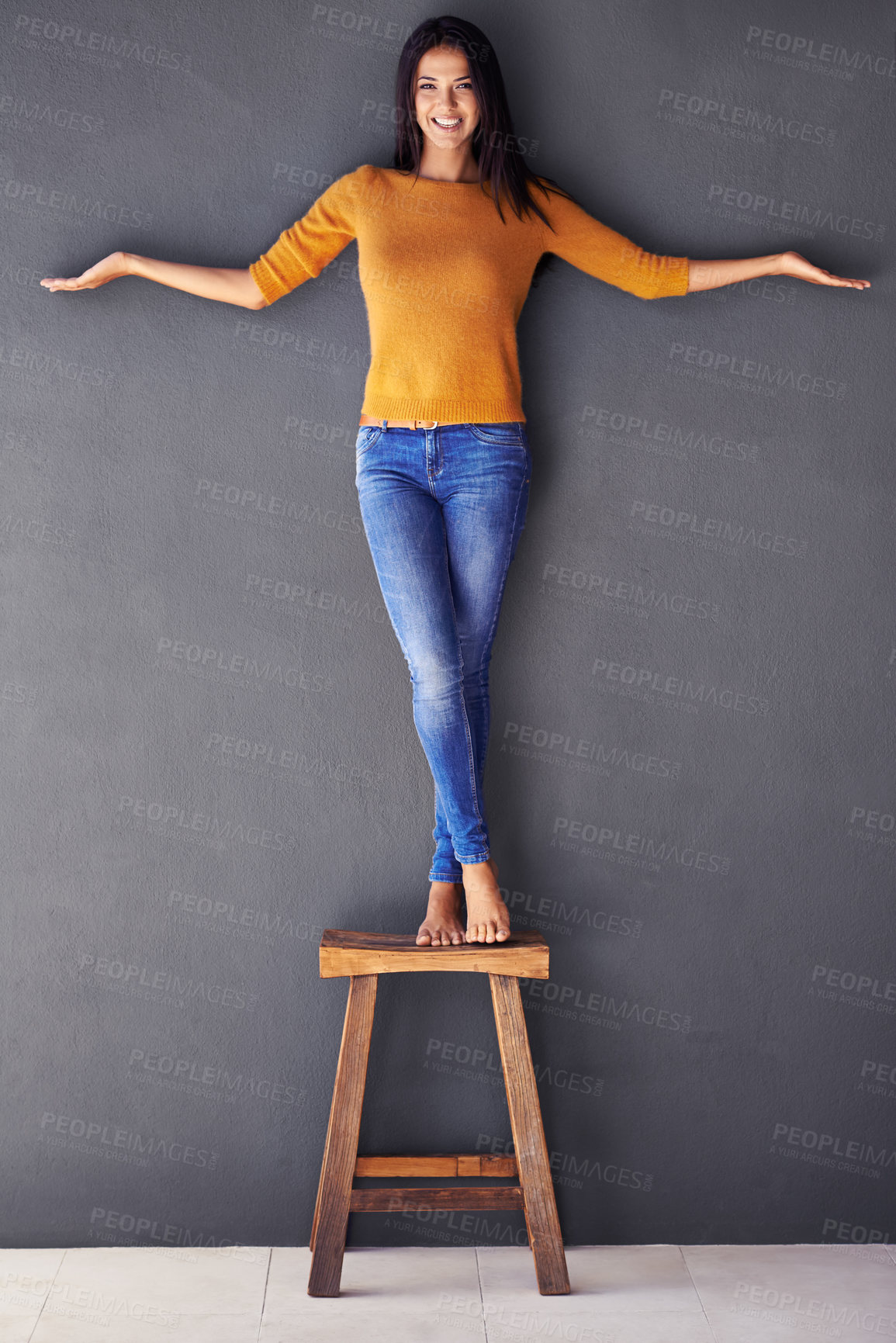 Buy stock photo Woman, fashion and stand on chair in portrait, smile and balance on wall background. Female person, modern clothing and happy lady on stool, barefoot and confidence in living room at home in house