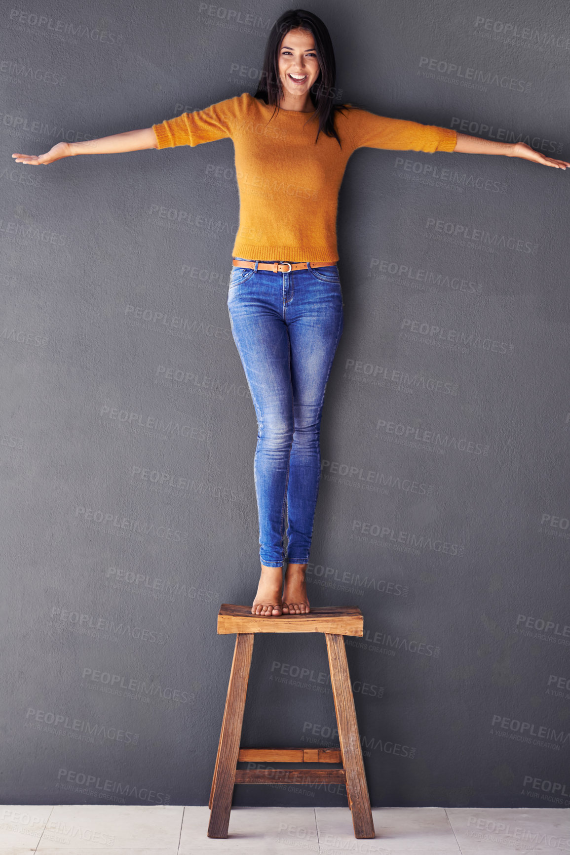 Buy stock photo Woman, confident and stand on chair in portrait, smile and fashion on wall background. Female person, clothes and happy lady on stool, apparel and trends in living room at home in house
