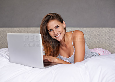 Buy stock photo Shot of an attractive young woman using her laptop while lying on the bed