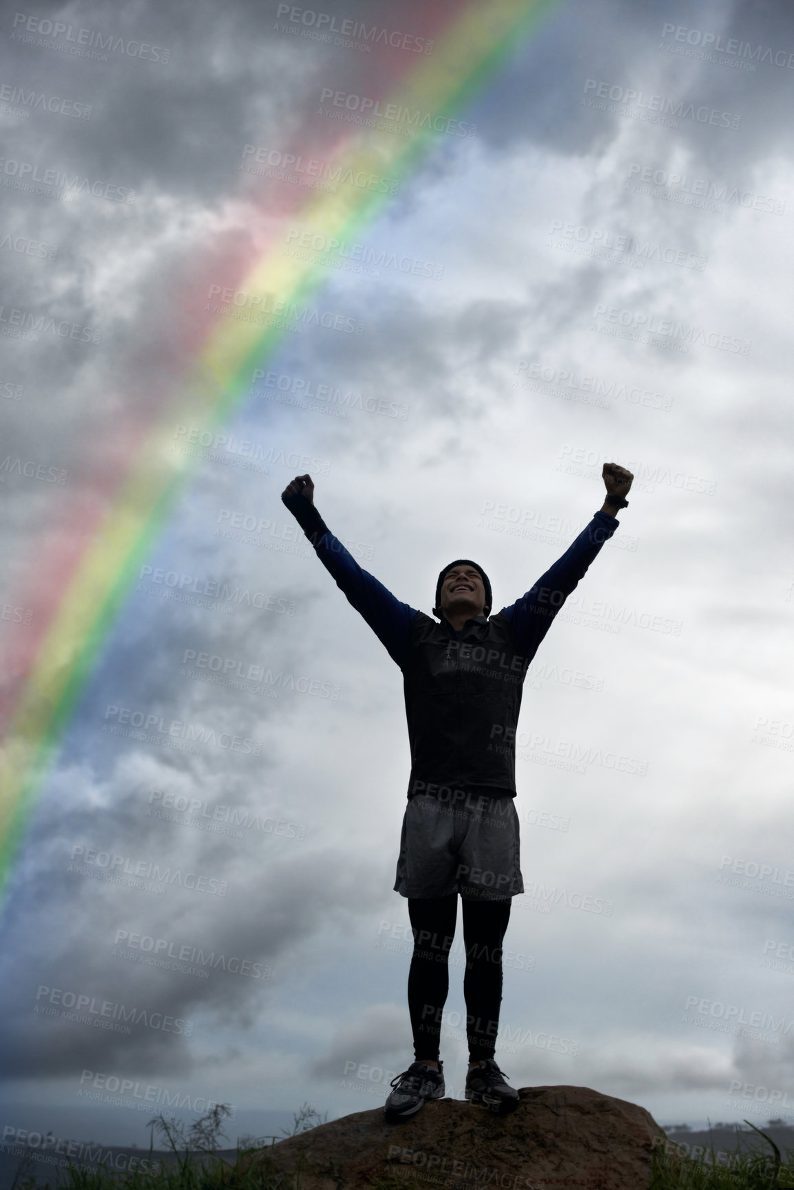 Buy stock photo Man, rainbow and cloudy sky in celebration for freedom, achievement or fitness standing on mountain. Active male person with fist pump in victory for workout, exercise or outdoor training success