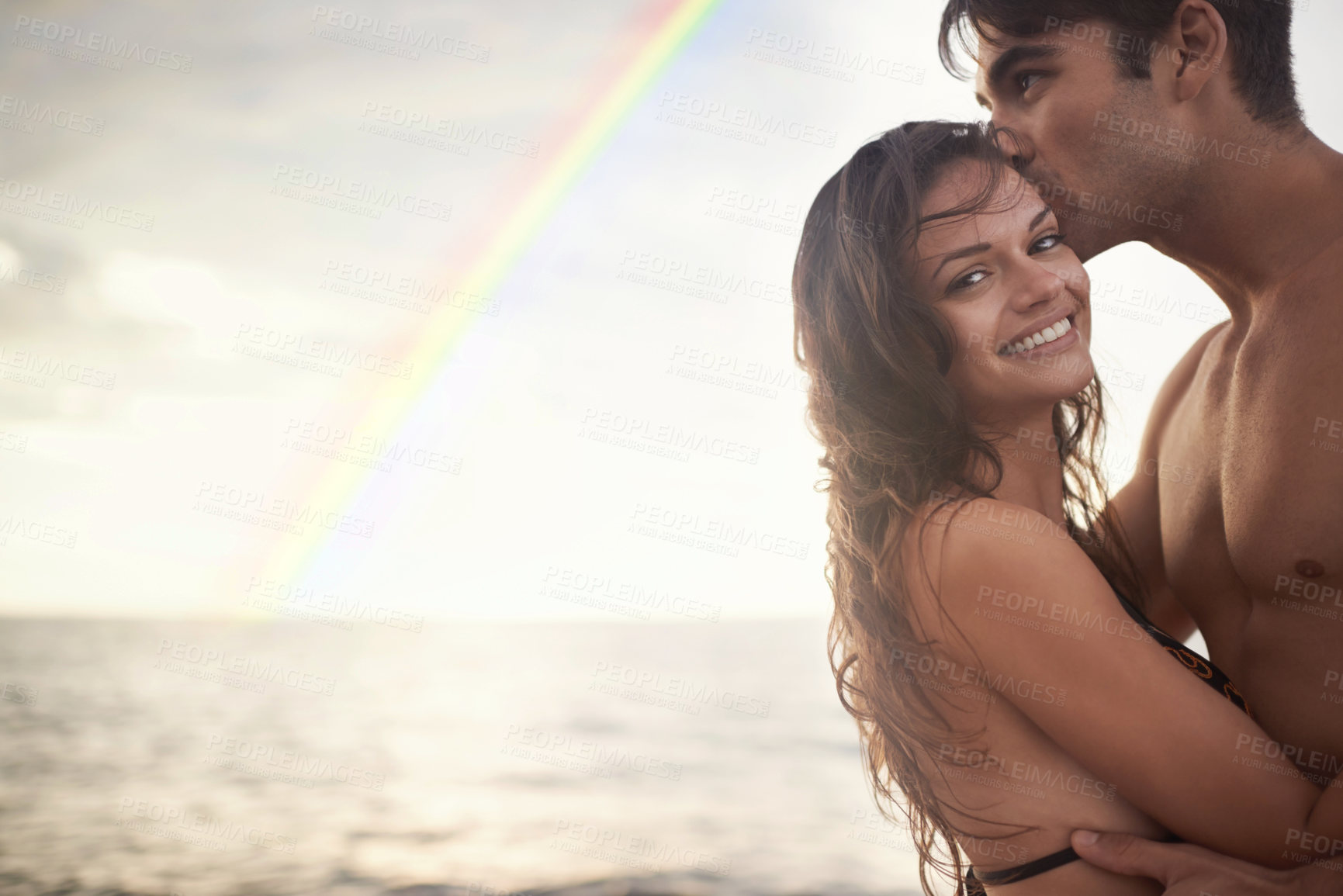 Buy stock photo Couple, hug and kiss by ocean, nature and rainbow with travel for happy people on vacation. Romantic adventure together, relax outdoor and bonding for love, care and trust in healthy relationship