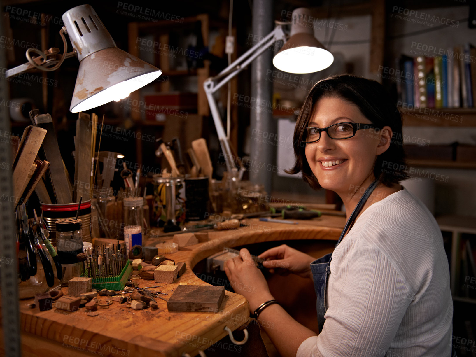 Buy stock photo Shot of a happy young woman sitting at a workbench