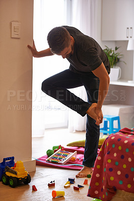 Buy stock photo Shot of a man grabbing his foot in pain after standing on a child's toy