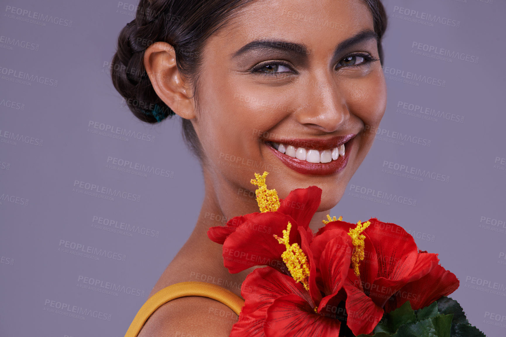 Buy stock photo Portrait, smile and woman with flowers for makeup, skincare or health isolated on a purple studio background in India. Face, person and cosmetics with bouquet for natural beauty with organic hibiscus