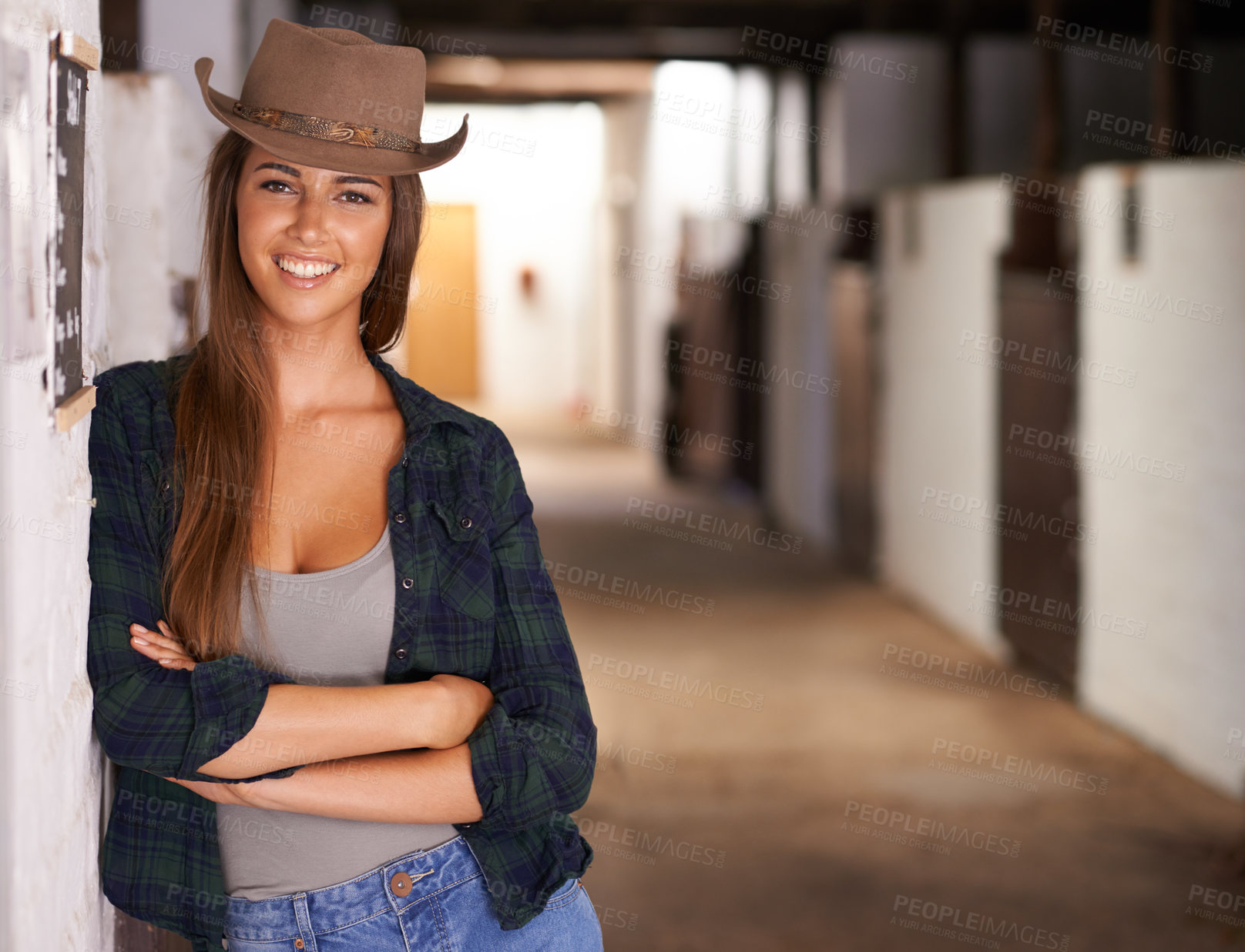 Buy stock photo A portrait of a beautiful young cowgirl leaning against a wall in a stable