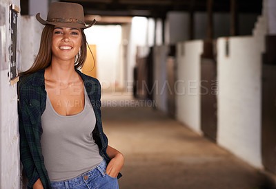 Buy stock photo A portrait of a beautiful young cowgirl leaning against a wall in a stable