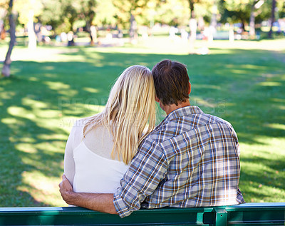 Buy stock photo Rearview of an affectionate young couple sitting on a park bench