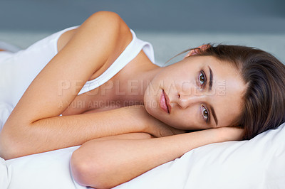 Buy stock photo A young woman looking sad while lying on her bed