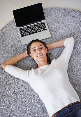 Buy stock photo Shot of a young woman lying on a rug next to a laptop