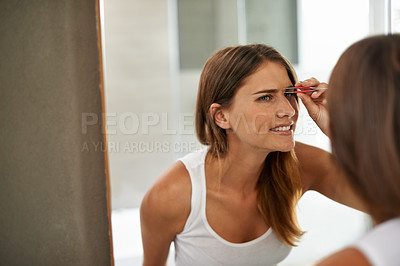 Buy stock photo Shot of a young woman painfully tweezing her eyebrows in a bathroom mirror