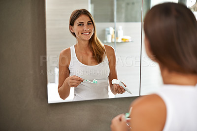 Buy stock photo Over the shoulder portrait of an attractive young woman brushing her teeth in a bathroom mirror