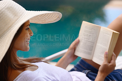 Buy stock photo Shot of a young woman reading a book by the poolside