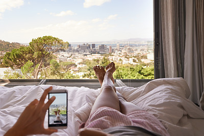 Buy stock photo Bed, phone and window view with feet, relax and photography for blog, review and screen in hotel. Woman, hand and smartphone for profile picture with cityscape, nature or social media app in bedroom