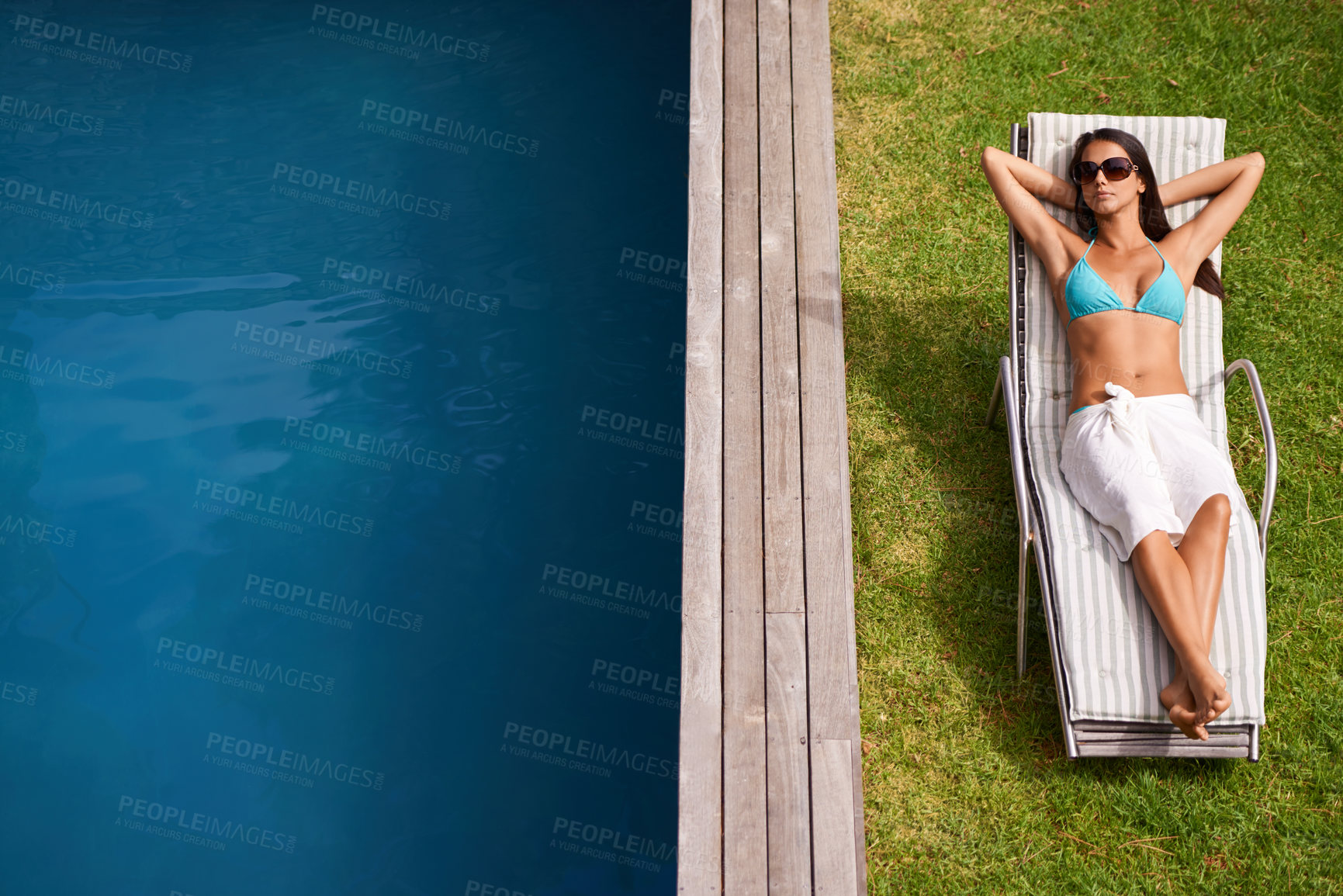 Buy stock photo A beautiful young woman relaxing in a lounge chair by a swimming pool