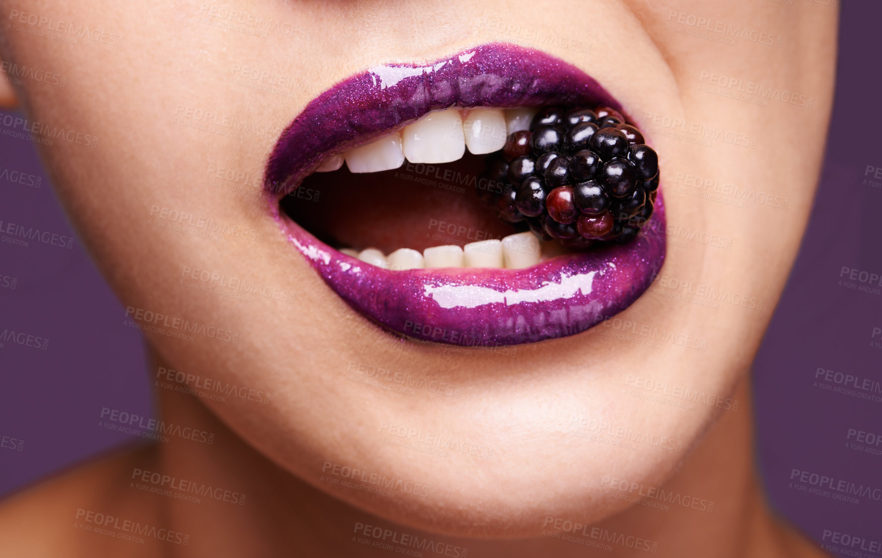 Buy stock photo Woman lips, purple lipstick with blackberry and makeup, shine and creativity with beauty isolated on studio background. Closeup of fruit between female model teeth, cosmetic product and cosmetology