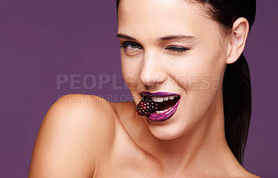 Buy stock photo A studio portrait of a beautiful young woman wearing purple lipstick and biting into a berry
