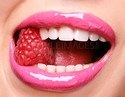 Buy stock photo Shot of a woman wearing pink lipstick and biting into a raspberry