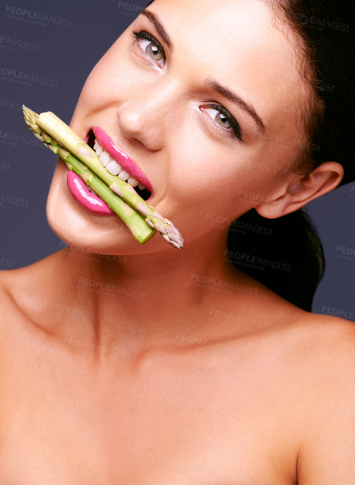 Buy stock photo Woman, lipstick and vegetables in mouth in portrait, beauty and nutrition for vegan cosmetic product in studio. Cruelty free makeup, cosmetology and asparagus with pink lip gloss on grey background