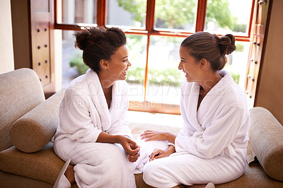 Buy stock photo Shot of two friends in bathrobes talking an laughing at a spa