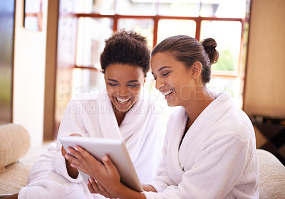 Buy stock photo Shot of two friends in bathrobes using a digital tablet at a spa