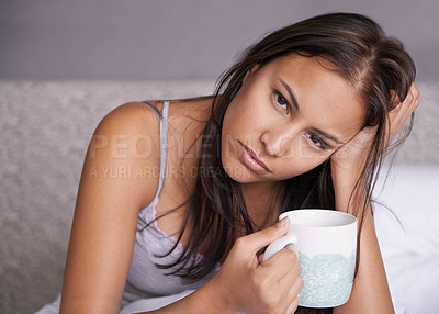 Buy stock photo Portrait of a tired young woman holding a cup of coffee while sitting in bed