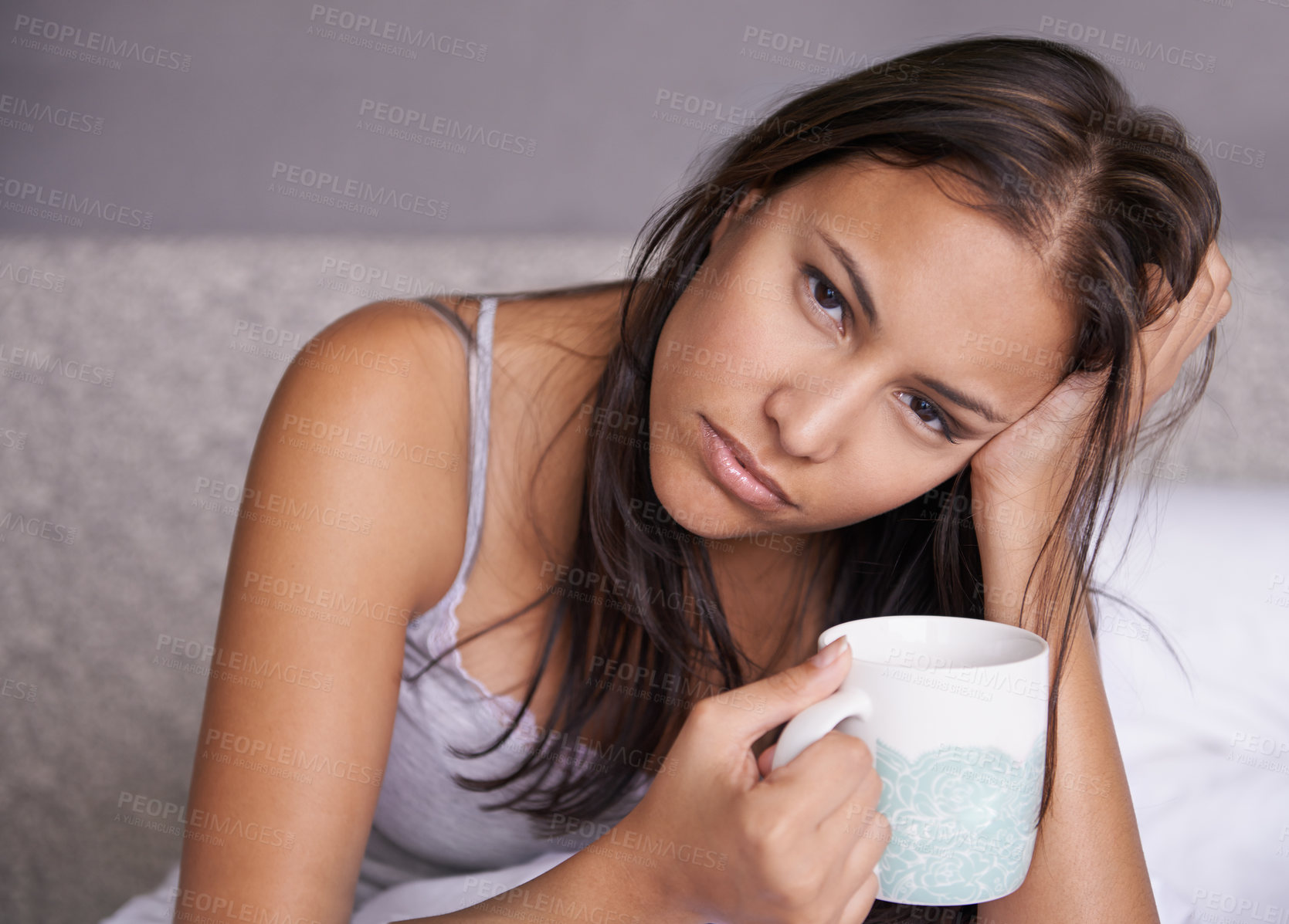 Buy stock photo Portrait of a tired young woman holding a cup of coffee while sitting in bed