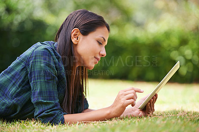 Buy stock photo Shot of an attractive young woman lying on the grass using a digital tablet