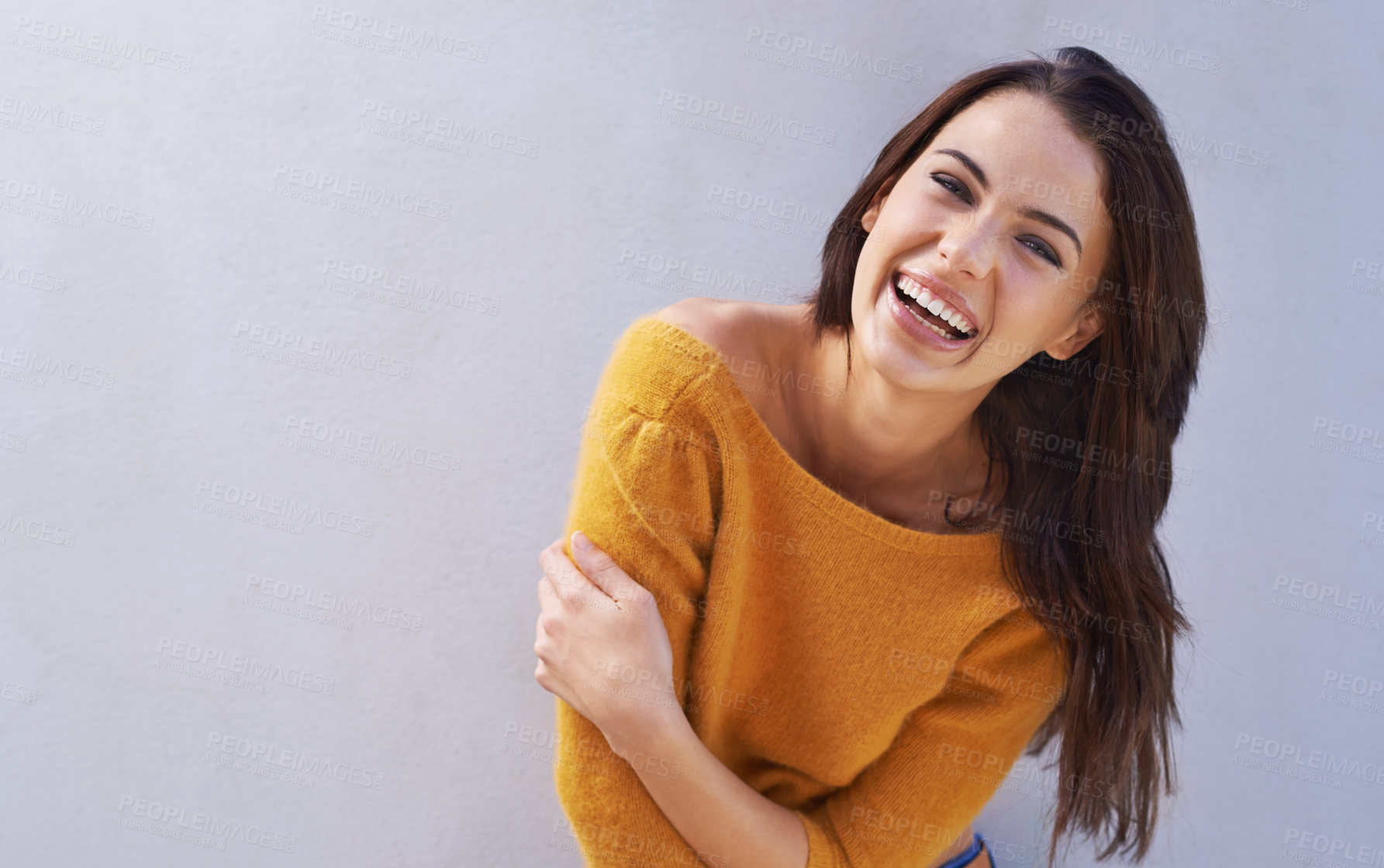 Buy stock photo Portrait of a beautiful young woman laughing while standing against a gray wall