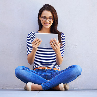 Buy stock photo Shot of an attractive young woman using a digital tablet while sitting cross-legged on the floor
