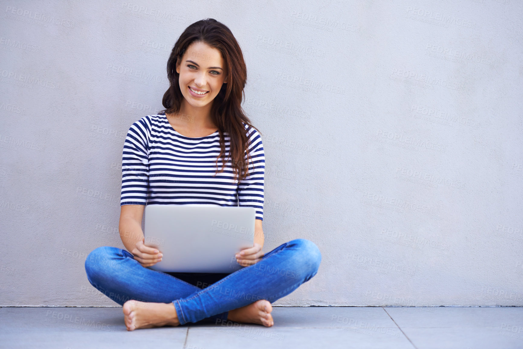 Buy stock photo Full-length shot of an attractive young woman sitting cross-legged using a laptop