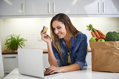 Buy stock photo Cropped shot of a young woman doing some online shopping with her groceries beside her