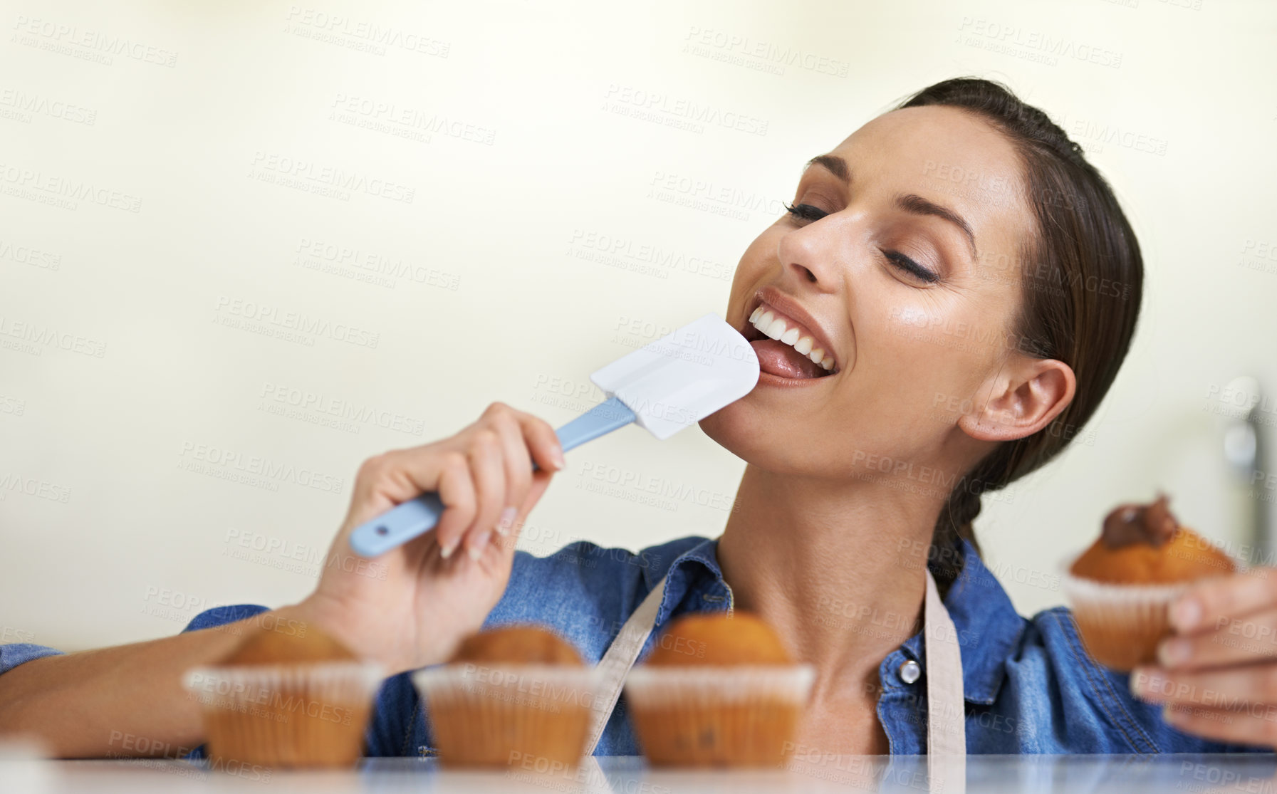 Buy stock photo Baking, cupcakes and woman with spatula in kitchen tasting sweet chocolate frosting for dessert. Cooking, eating and young female baker working on muffins and licking tool at home or apartment.